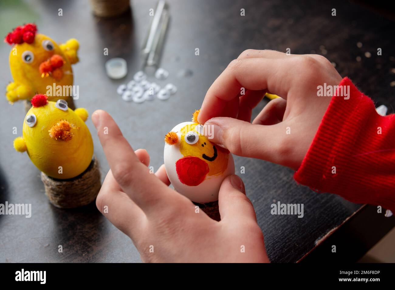 A girl decorates an egg for the Easter holiday by carefully gluing funny eyes to it Stock Photo