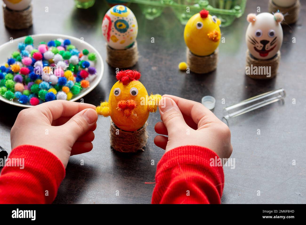 Children's hands made a chicken craft out of an egg, there are other figures in the background Stock Photo