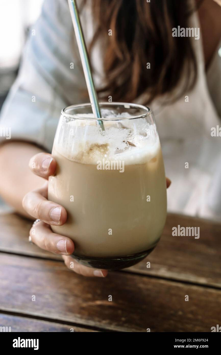 Ice latte in hand. A glass glass of cold coffee drink with milk in the hand of a girl in a summer town coffee shop on the street. Drink, lifestyle, city concept. High quality photo Stock Photo
