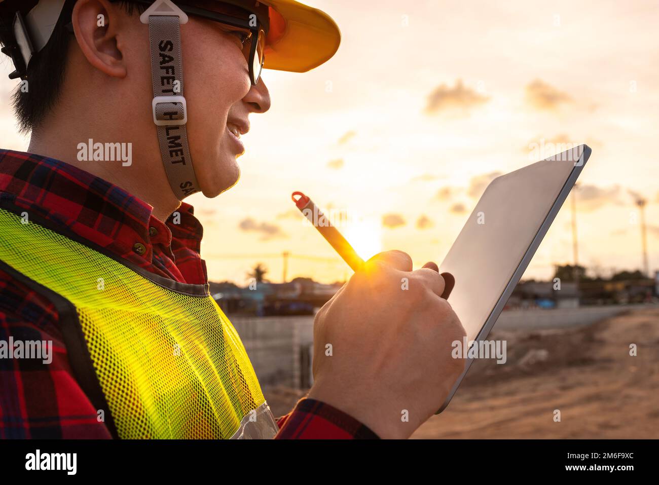 asian technician civil engineer use tablet with smart pen technology on transport site construction to inspect blueprint engineering work online with Stock Photo