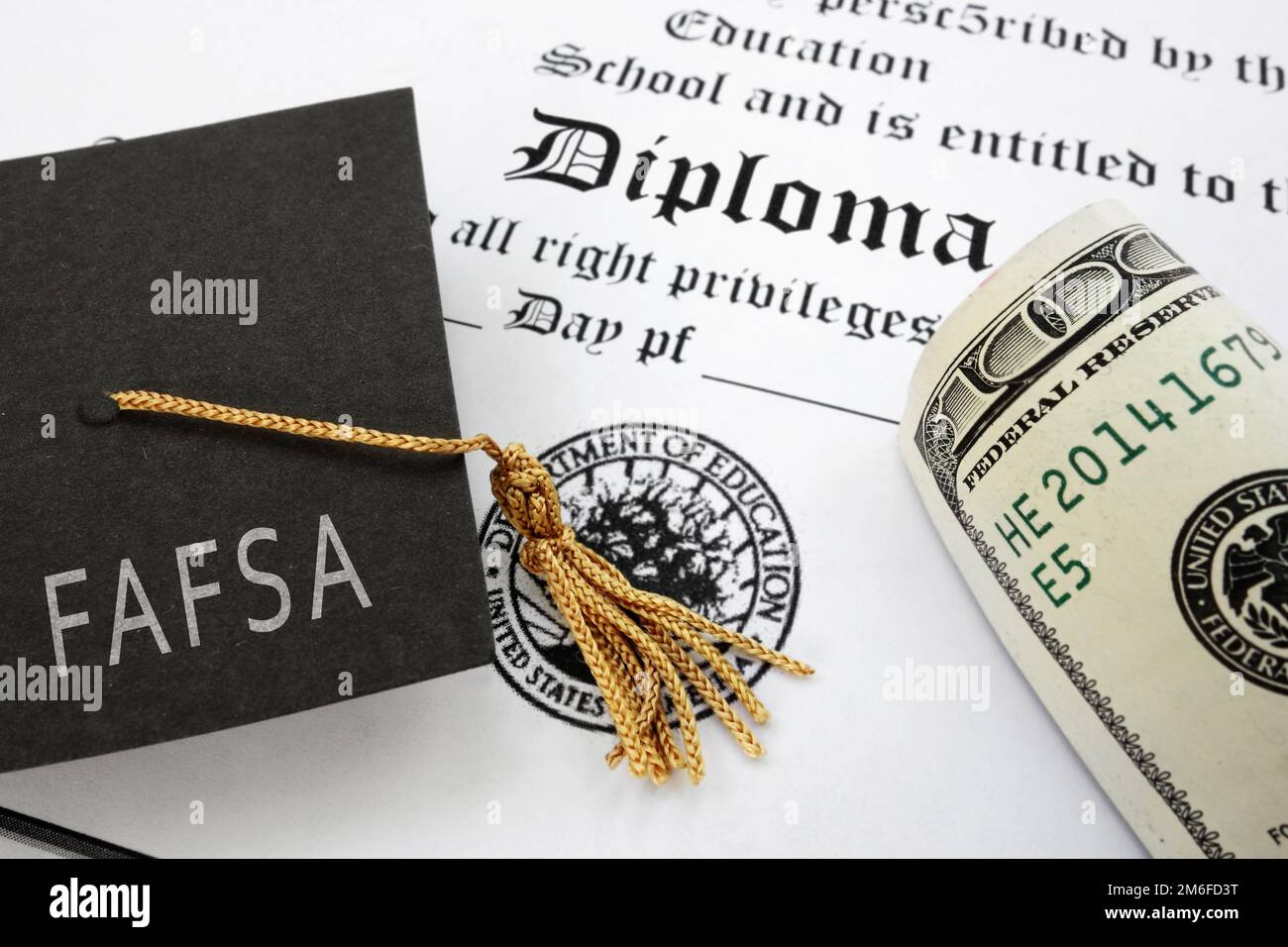 FAFSA (Free Application for Federal Student Aid) text on graduation cap with diploma and money Stock Photo