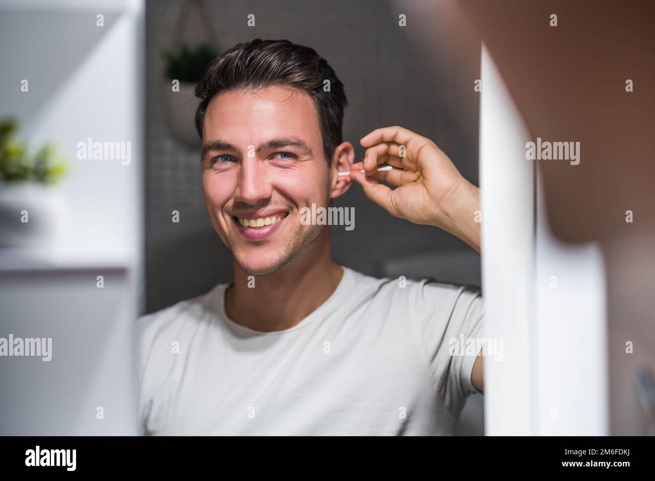 Man cleaning ear while looking himself in the mirror. Stock Photo