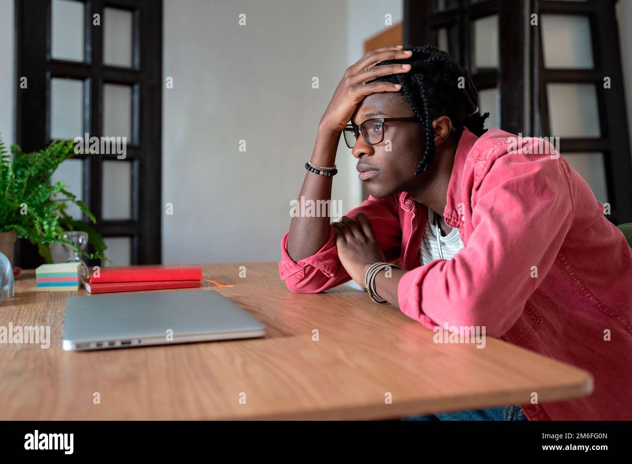 Upset young African guy freelancer touching forehead thinking about personal problems at workplace Stock Photo