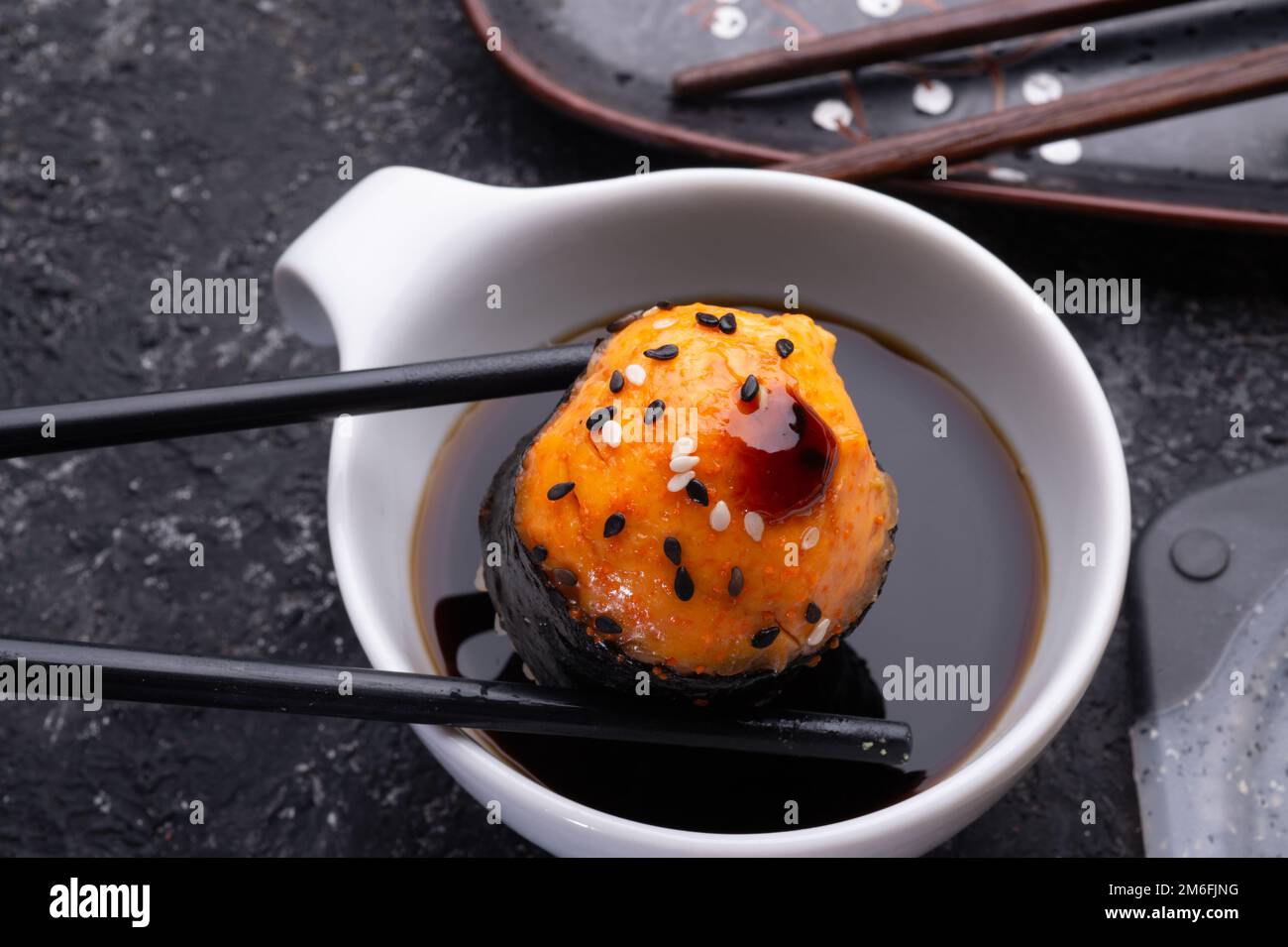 Baked sushi roll holding by sticks under soy souce. sushi rolls served at grey  tray. flat lay. close up Stock Photo