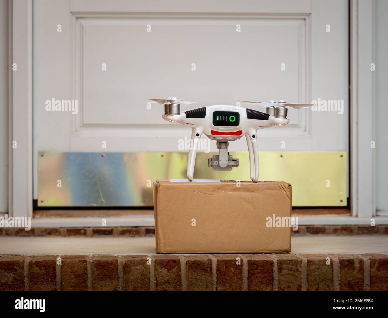 Drone delivering package to the front door of a house. Residential package delivery via unmanned aerial vehicle. Stock Photo