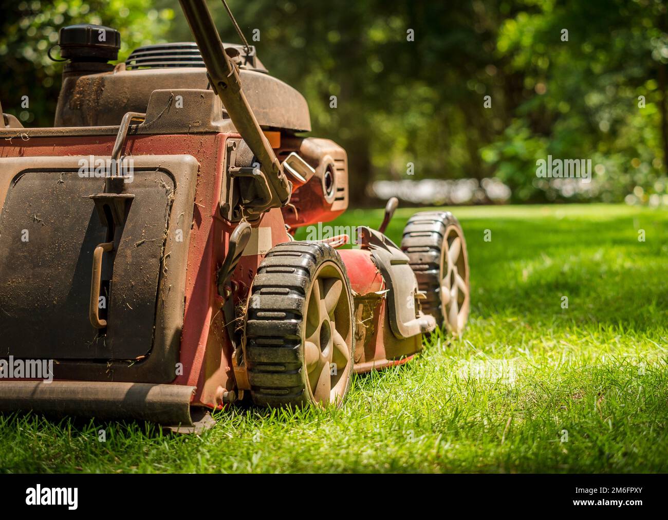 Grungy lawn mower in green grass lawn. Walk behind gas powered