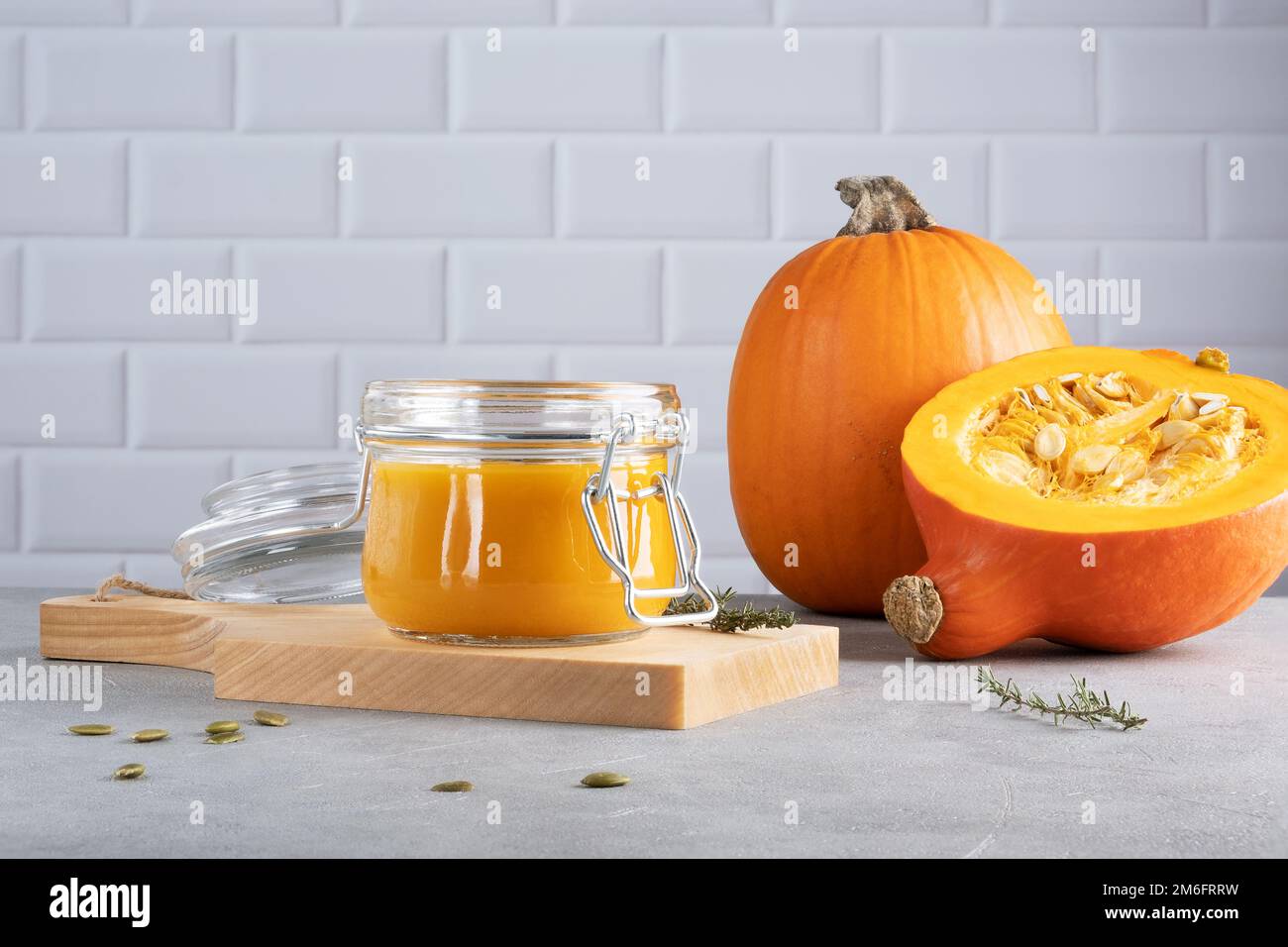 Pumpkin puree soup with pumpkin seeds and thyme in a glass jar on a wooden kitchen board. Ripe pumpkin. Healthy diet. Selective focus. Stock Photo