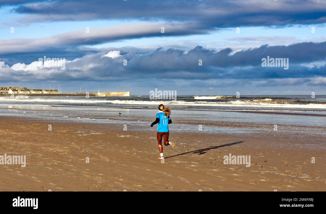 Lossiemouth East Beach Moray coast Scotland a blue sky white clouds and surf and a runner on the sands in winter Stock Photo