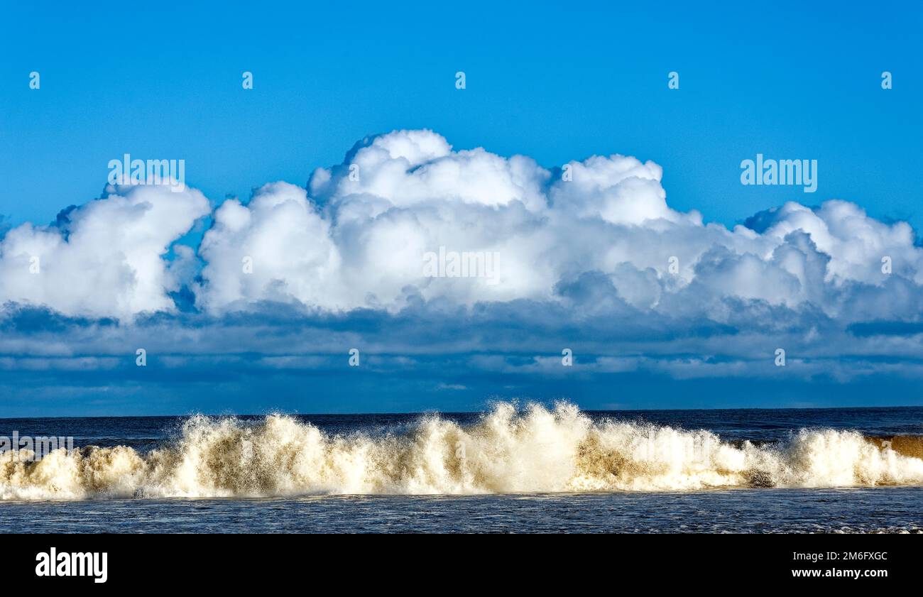 Lossiemouth East Beach Moray coast Scotland blue sky white clouds and massive surf from a breaking wave in winter Stock Photo