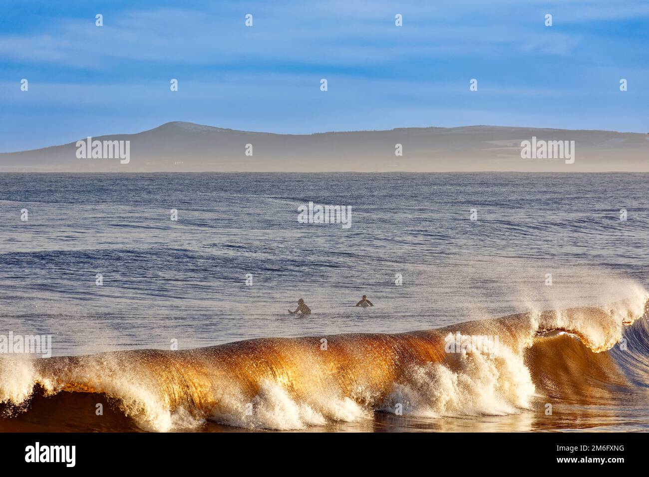 Lossiemouth East Beach Moray coast Scotland colourful curling waves with spray and two surfers waiting for a higher wave Stock Photo