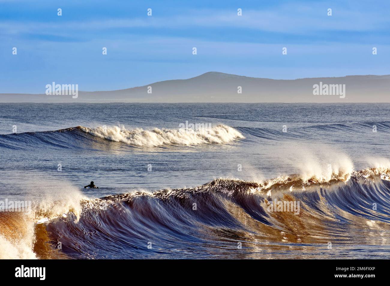 Lossiemouth East Beach Moray coast Scotland curling waves with spray and a surfer waiting for a wave Stock Photo