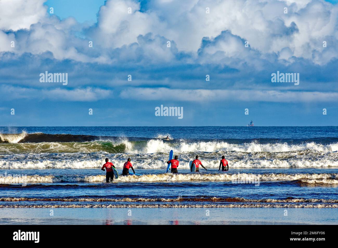 Lossiemouth East Beach Moray coast Scotland five surfers from the New Wave Surf School heading into the sea and breaking waves Stock Photo