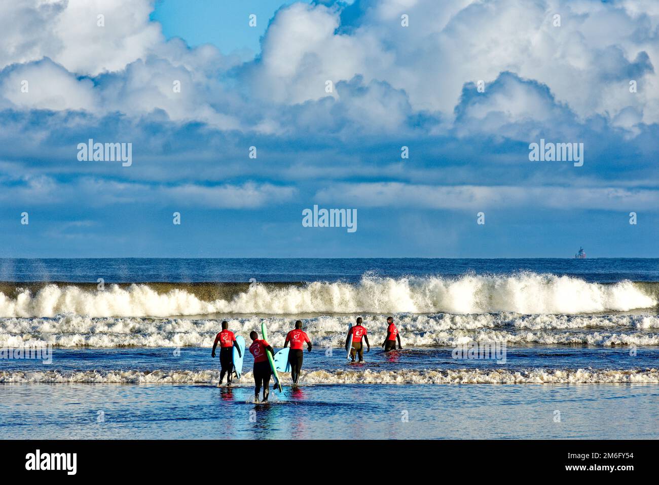 Lossiemouth East Beach Moray coast Scotland five surfers from the New Wave Surf School heading into the sea and waves Stock Photo