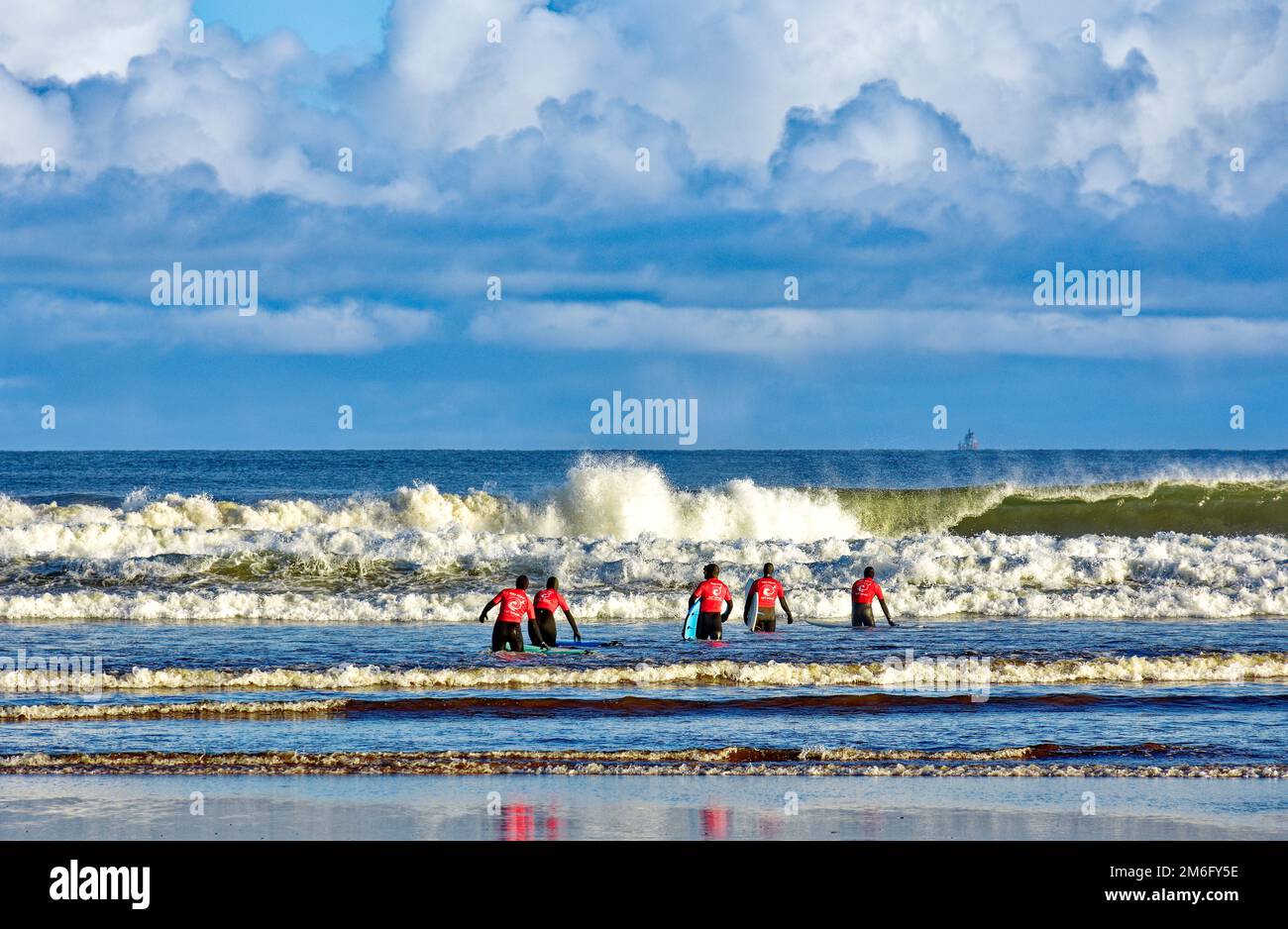 Lossiemouth East Beach Moray coast Scotland five surfers in red from the New Wave Surf School heading into the sea and breaking waves Stock Photo