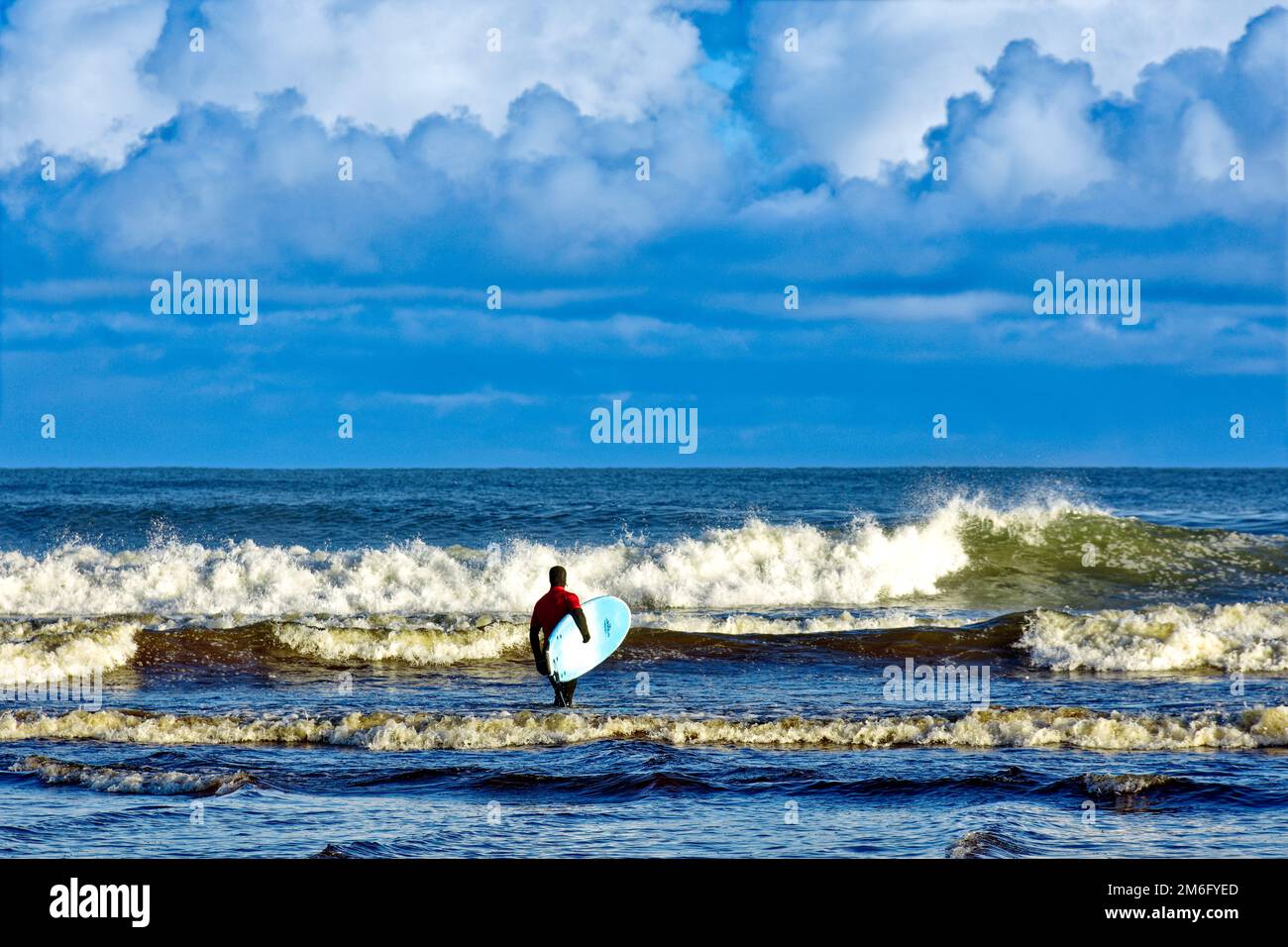 Lossiemouth East Beach Moray coast Scotland lone surfer in red from the New Wave Surf School heading into the sea and breaking waves Stock Photo