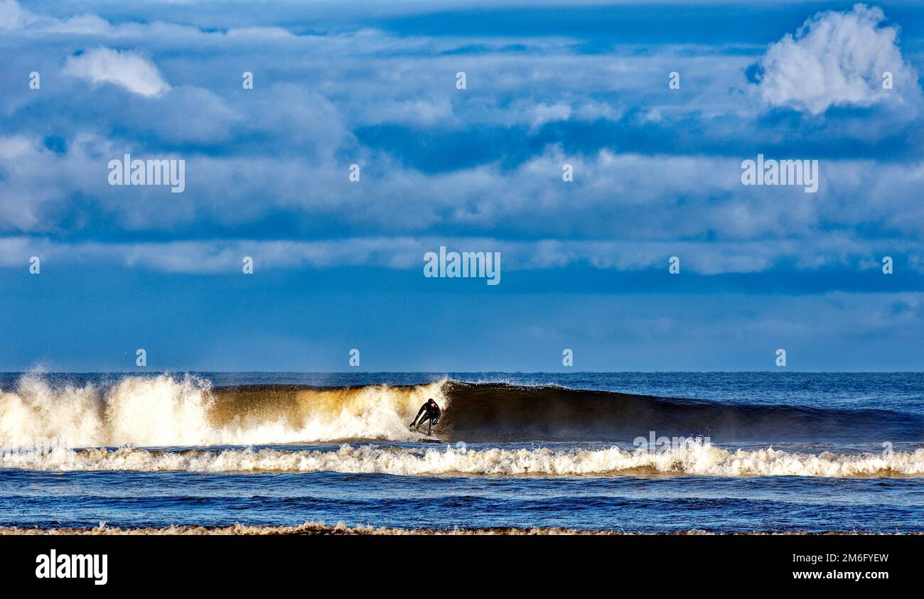 Lossiemouth East Beach Moray coast Scotland lone surfer on a breaking wave in winter Stock Photo