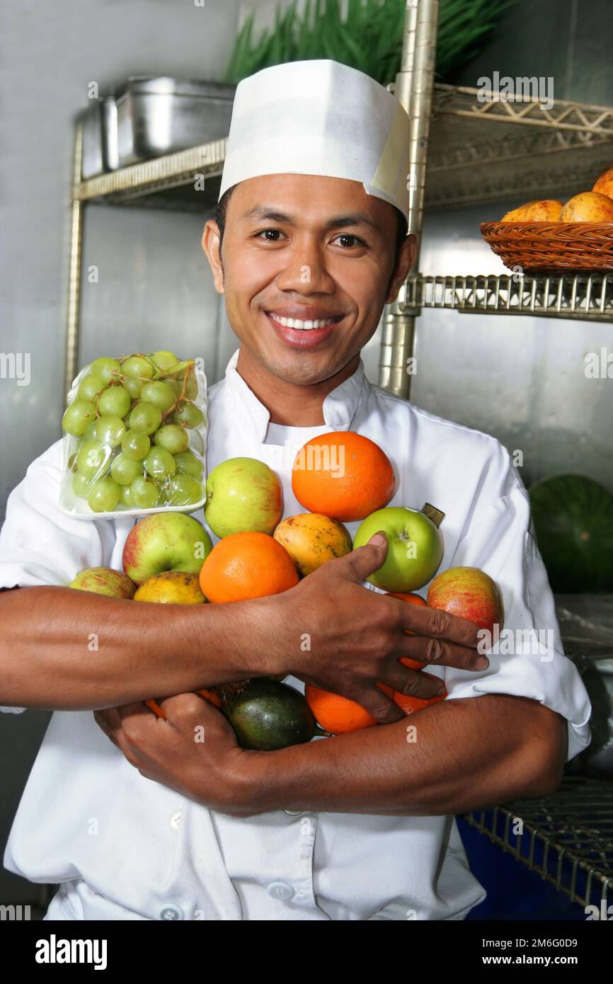 young chef holding fruits smiling look at camera in fridge Stock Photo