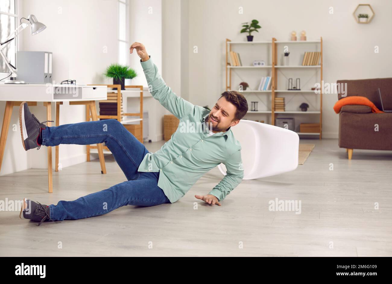 Man falls down on the floor as he misses the chair or slips on the slippery floor surface Stock Photo