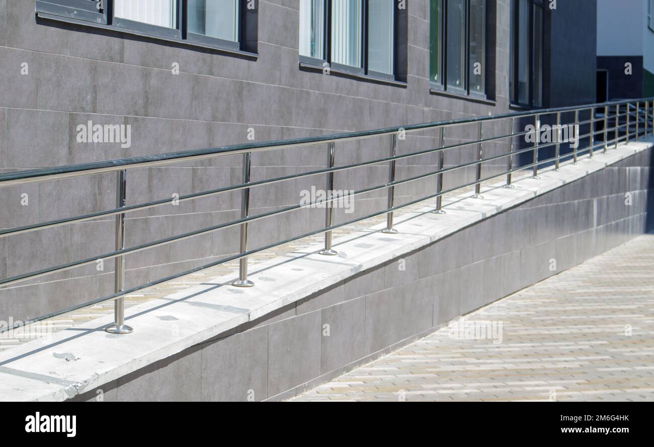 A ramp with stainless steel handrails for wheelchairs, bicycles and strollers with children in front of the building. Handrail f Stock Photo