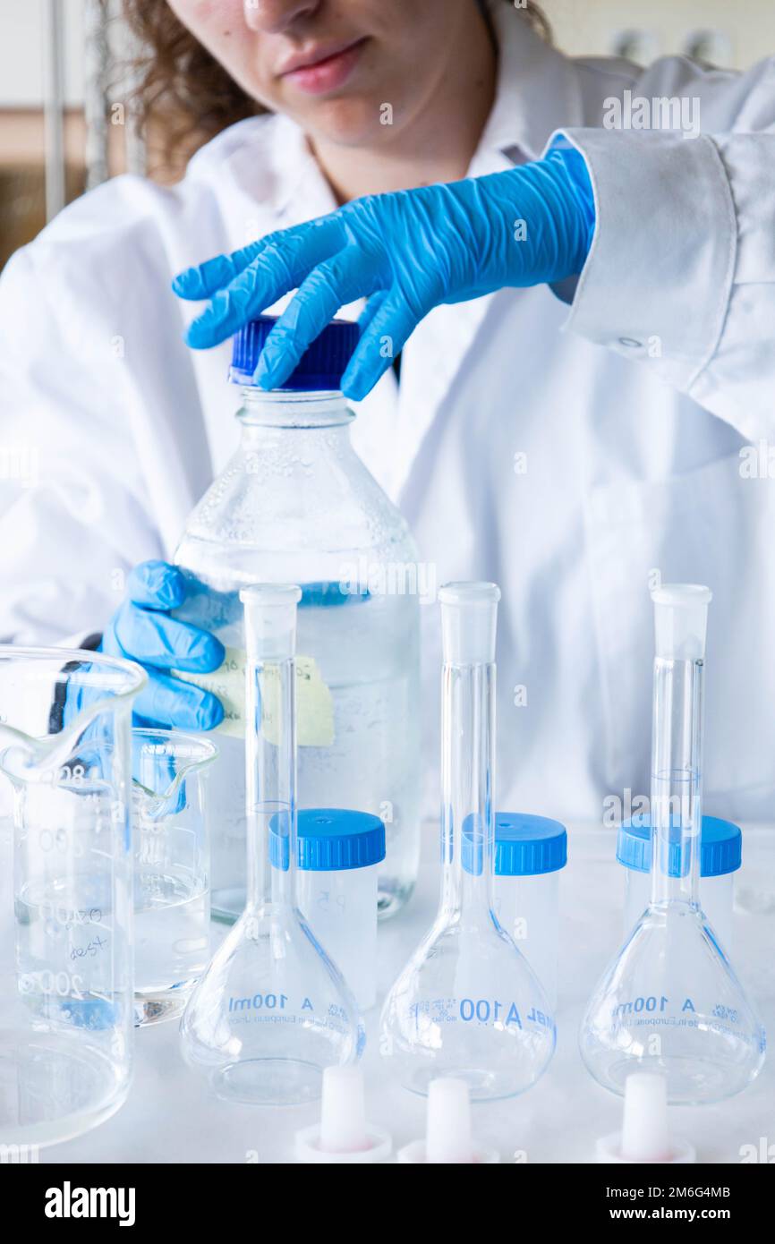Close-up left handed female scientist opening a sample jar with blue gloves and equipment. Laboratory technician working. Development and research. Stock Photo