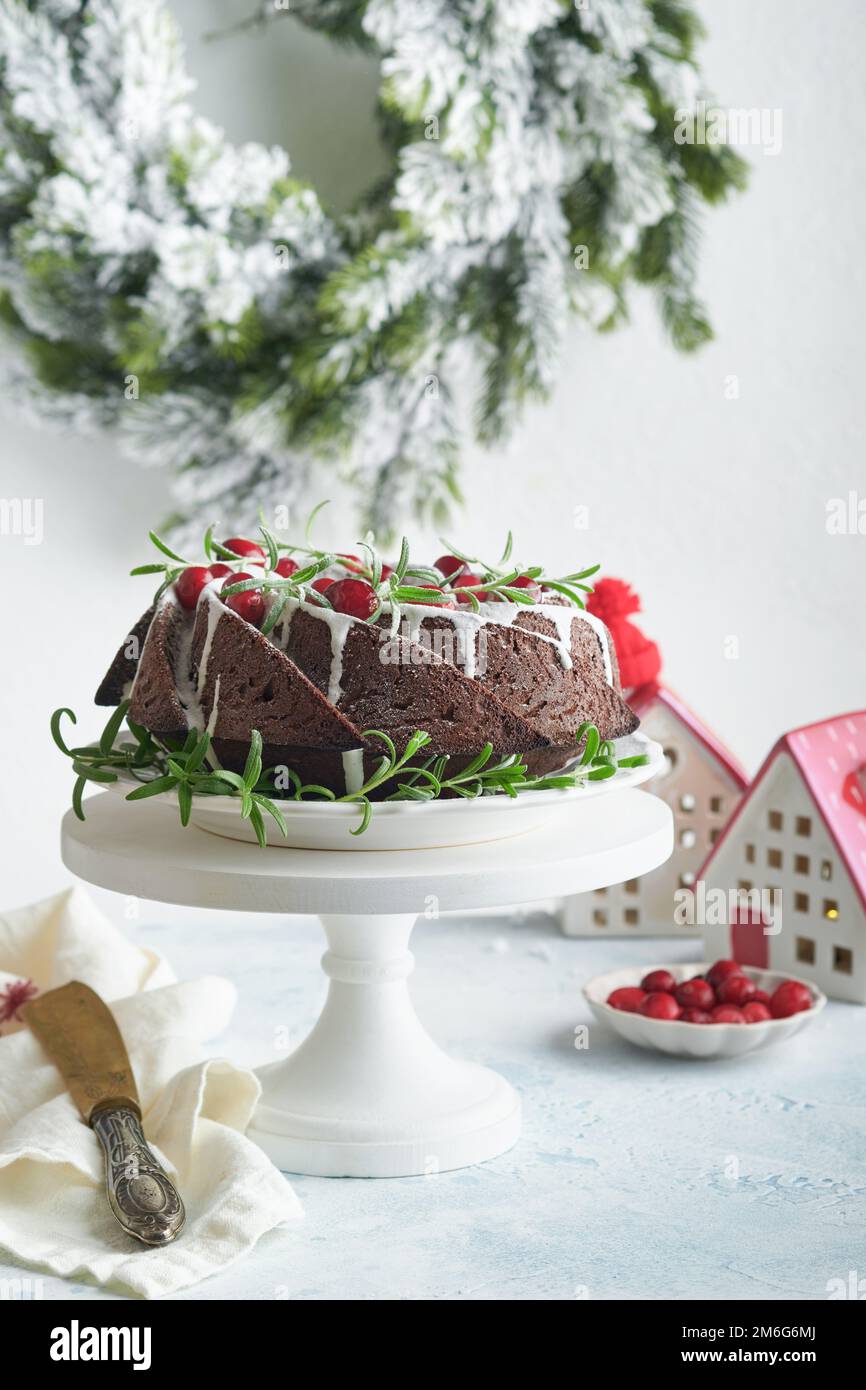 Christmas chocolate bundt cake. Traditional Christmas fruit cake with white glaze, cranberries and rosemary on white stand with Christmas decoration. Stock Photo