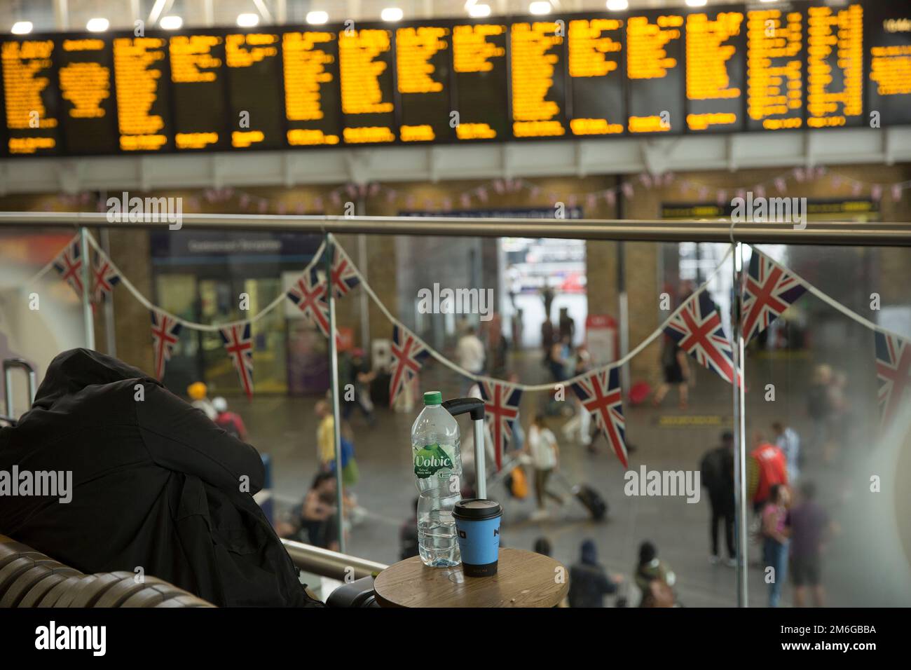 Backdropped by an electric timetable, a person sleeps on the bench at King's Cross station in London during a rail strike over pay and conditions. Stock Photo