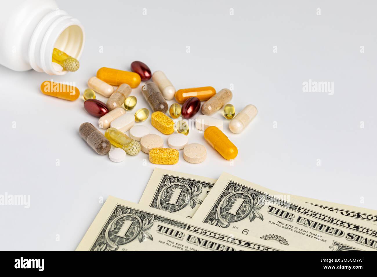 Pill bottle of vitamins and nutritional supplements with cash money isolated on white background. Wellness, health care and nutrition concept. Stock Photo