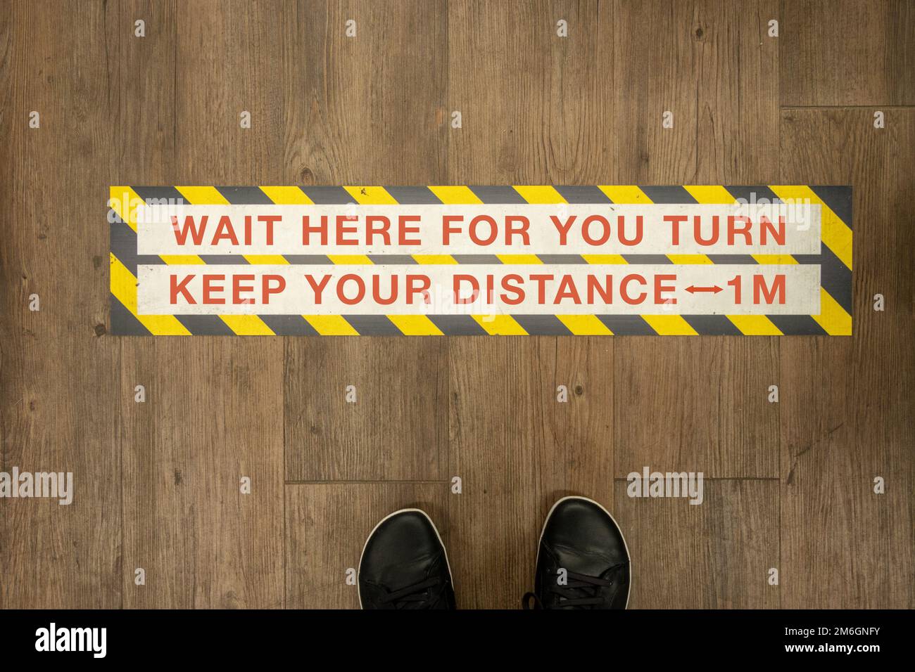 Wait your turn, keep your distance sign on a store floor Stock Photo