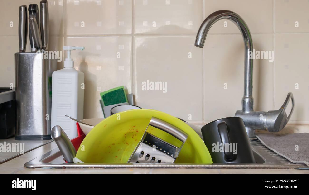 The kitchen utensils in the wash basin need to be washed. A pile of dirty dishes in the kitchen sink. Kitchen utensils need wash Stock Photo