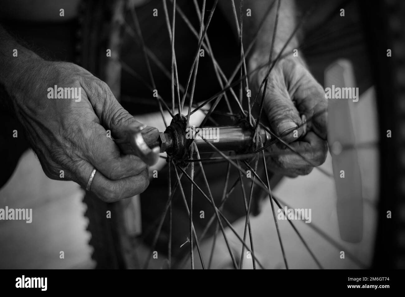 The old man working on a motorcycle tire with tools in close view in a service shop using fingers in hands Stock Photo