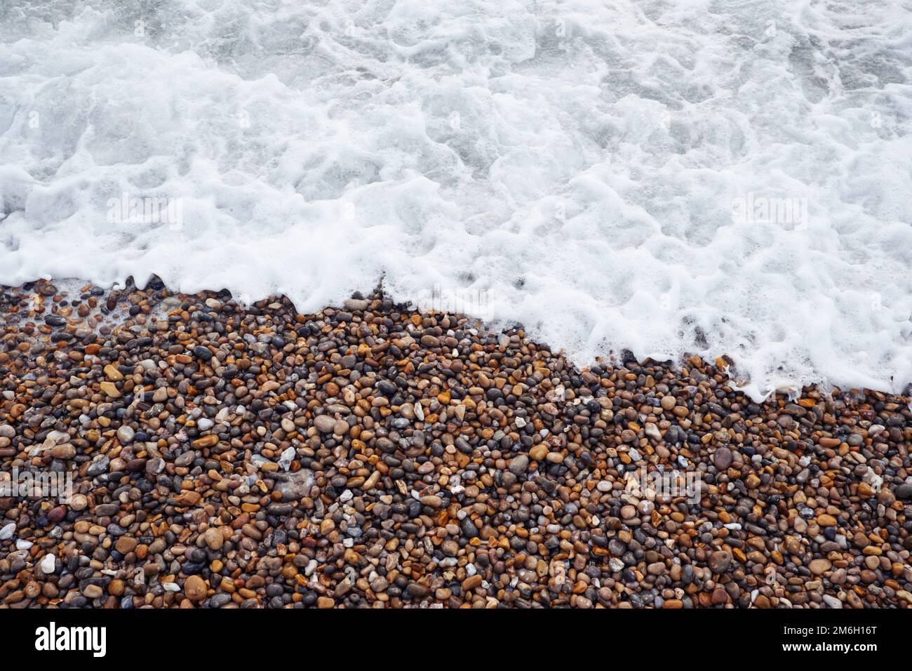 A close up as the foamy sea surf washes up over a people beach on the
