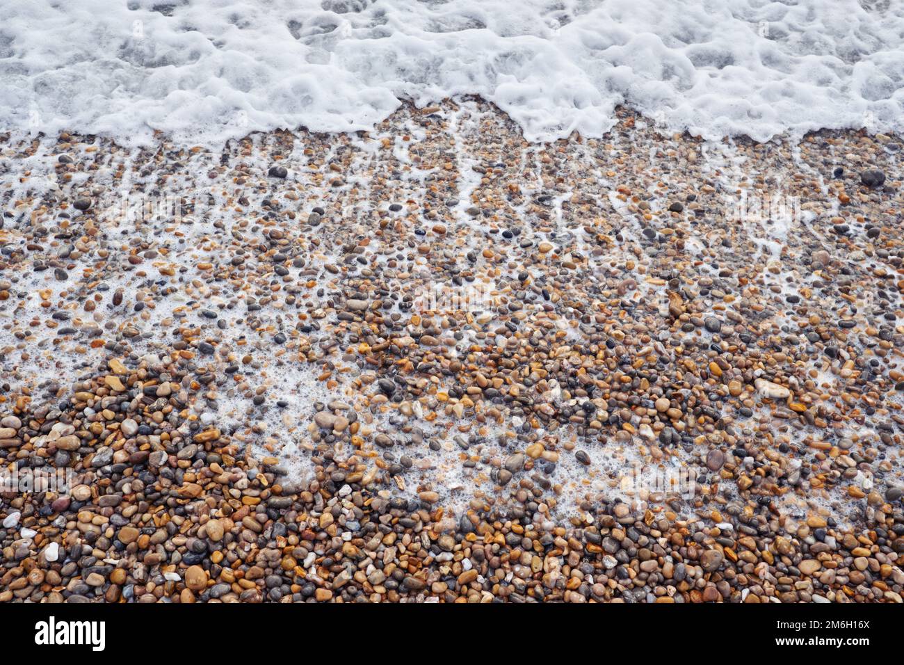 A close up as the foamy sea surf washes up over a people beach on the English south coast Stock Photo