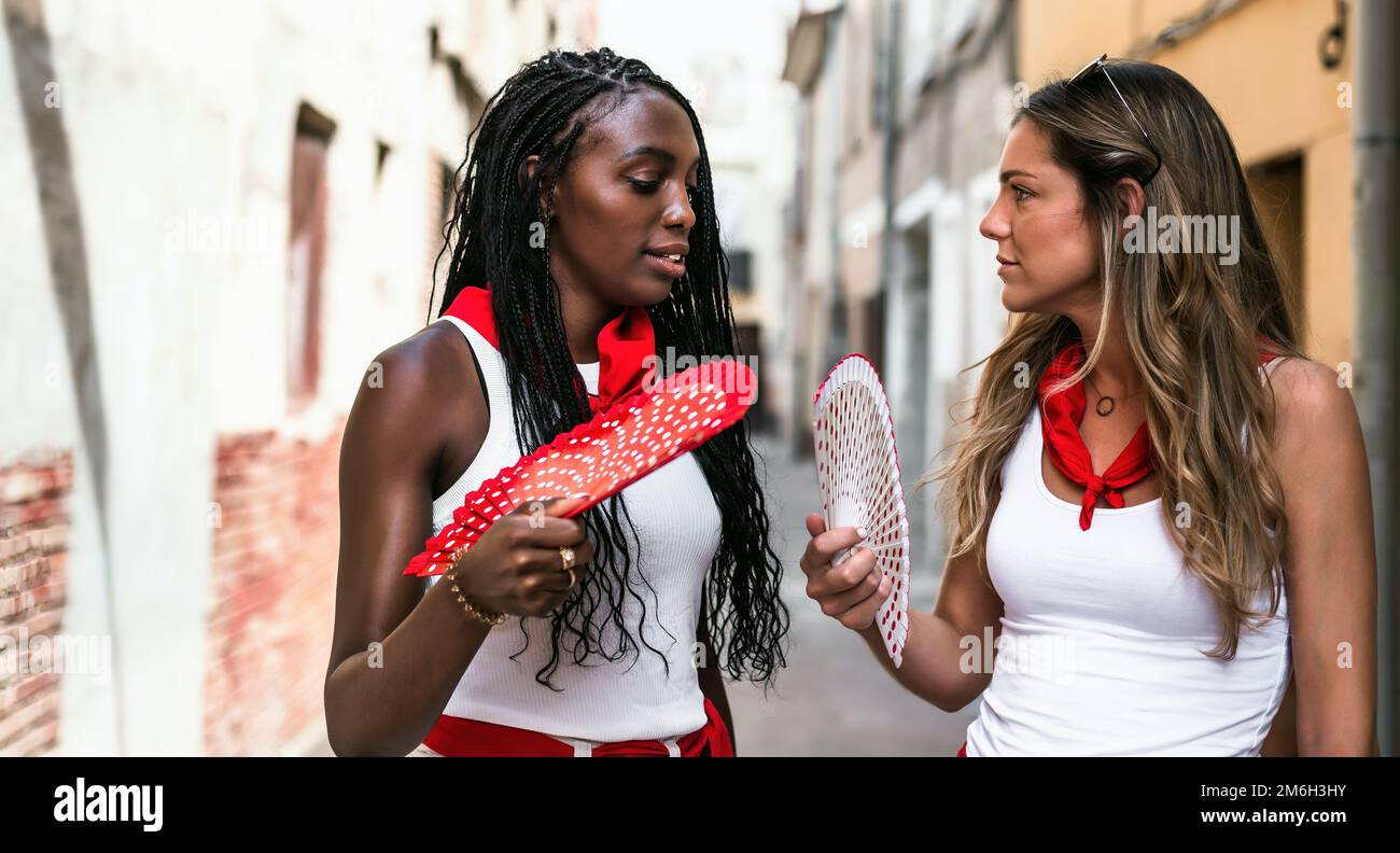 two young caucasian and black friends talk in the street with a certain intimacy during the festivities of a town in spain. concept of friendship, Stock Photo
