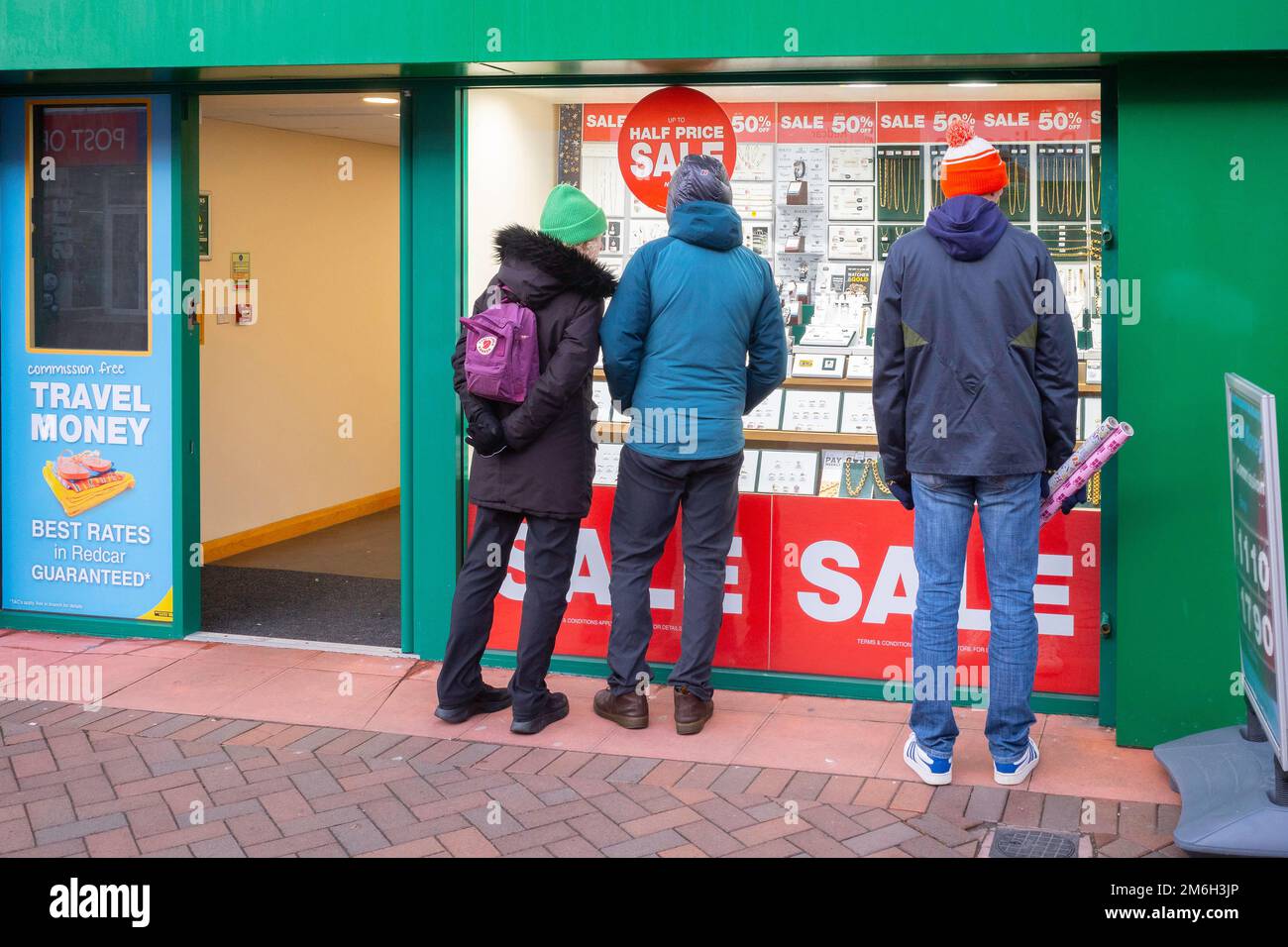 Three young adults window shopping in a pawnbrokers shop displaying jewelery at attractively reduced prices after Christmas in Redcar Cleveland Stock Photo