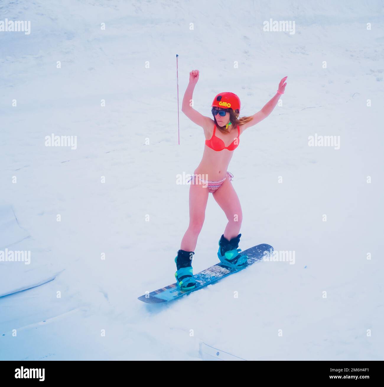 Russia, Sochi 11.05.2019. A beautiful girl in an orange swimsuit and helmet rides a snowboard down the slope with her hands up. Stock Photo