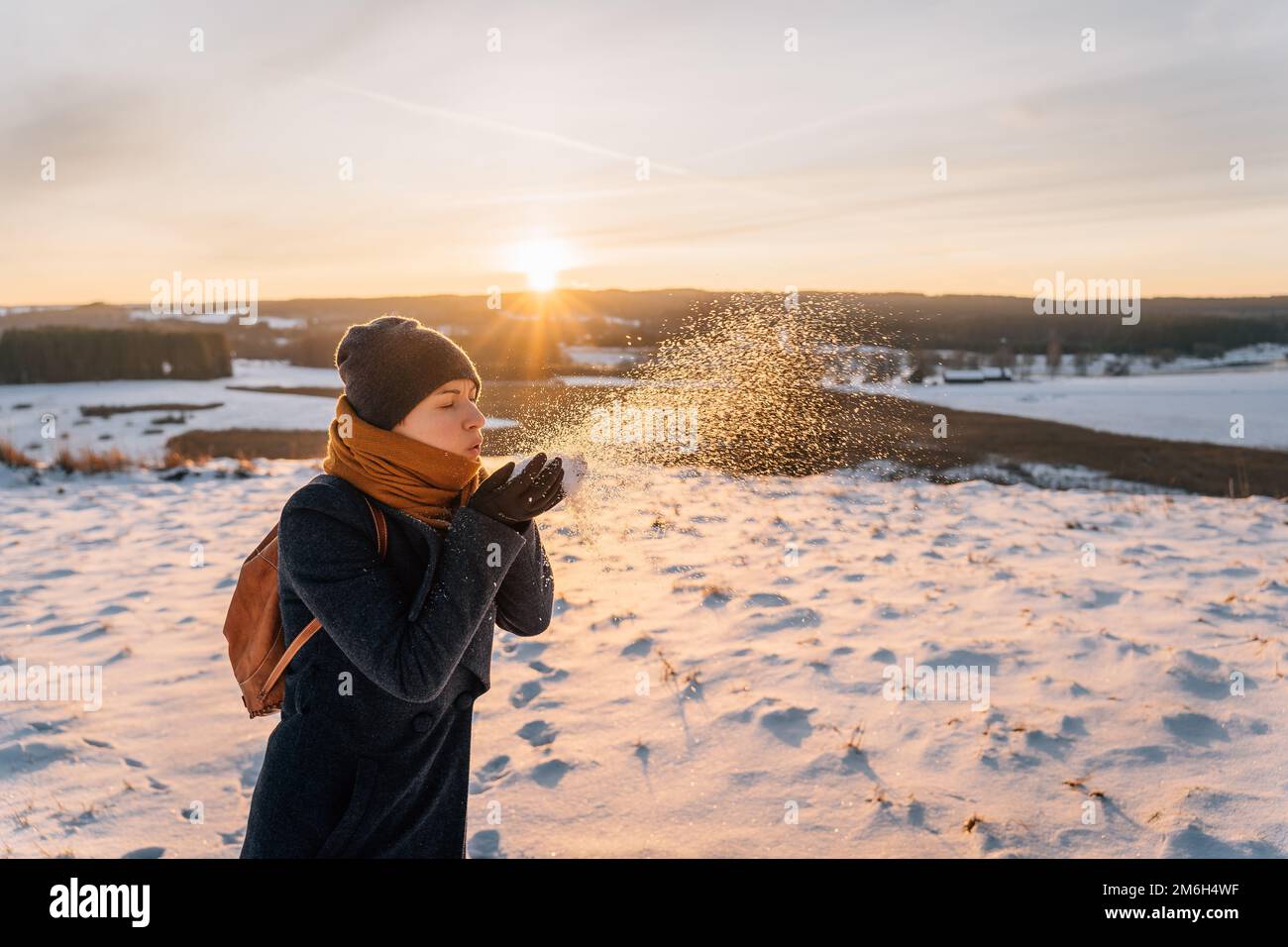 A woman in a coat wrapped in a scarf blows snow off her hands. Stock Photo
