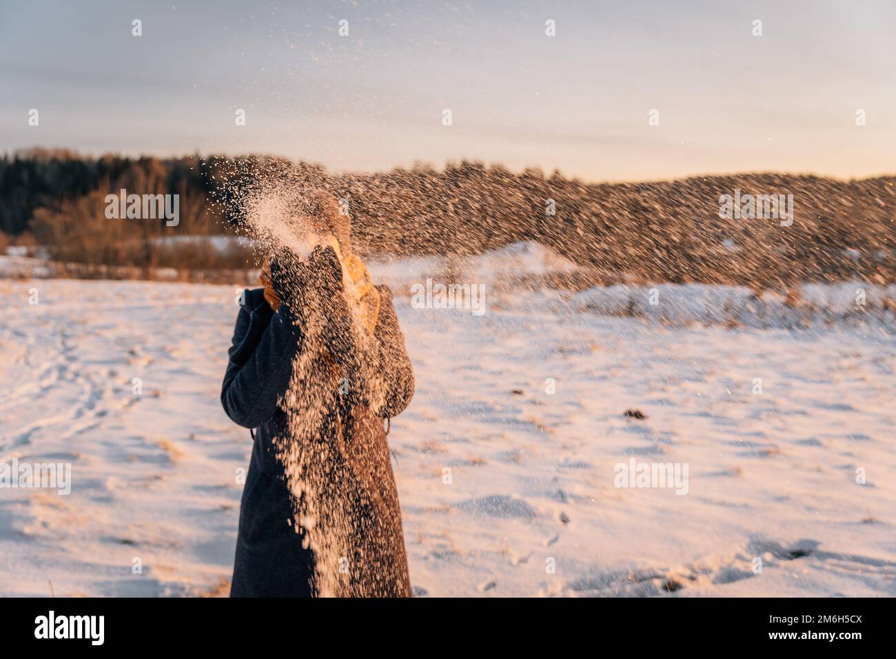 An unidentified woman throws snow in a snow-covered field. Stock Photo