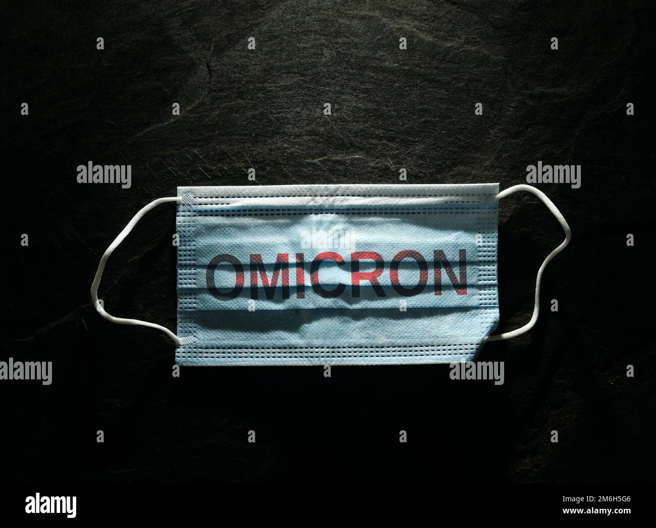 Blue surgical face mask with Omicron text on black background  --  Coronavirus PPE Stock Photo