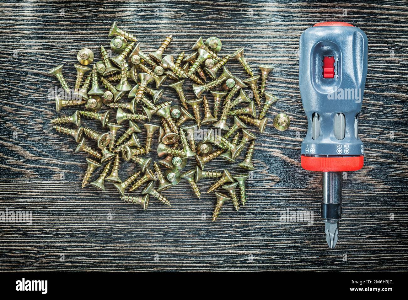 Screwdriver tapping screws on wooden board. Stock Photo