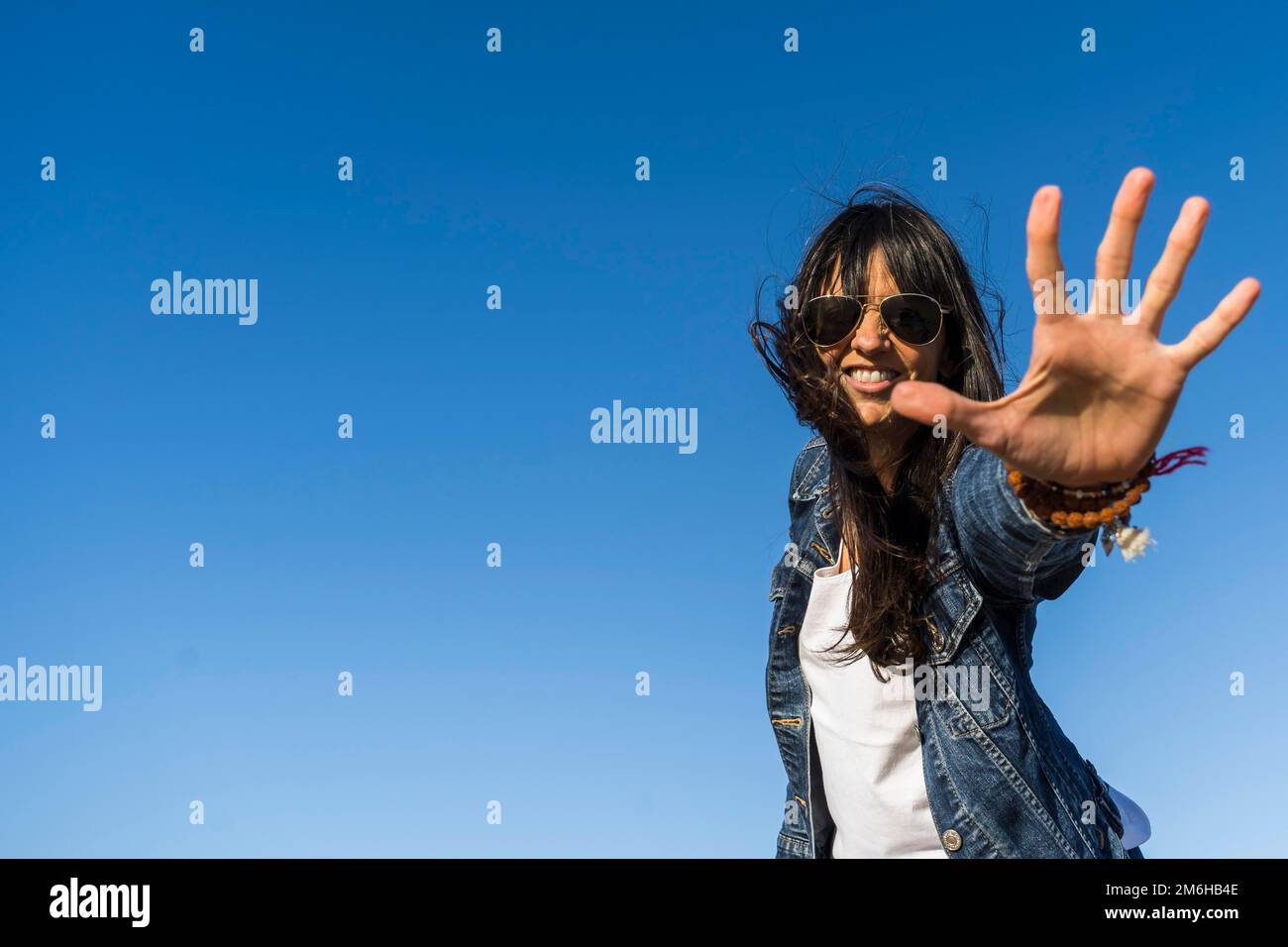 Low angle view of a similing woman while showing her hand. Blue sky background Stock Photo