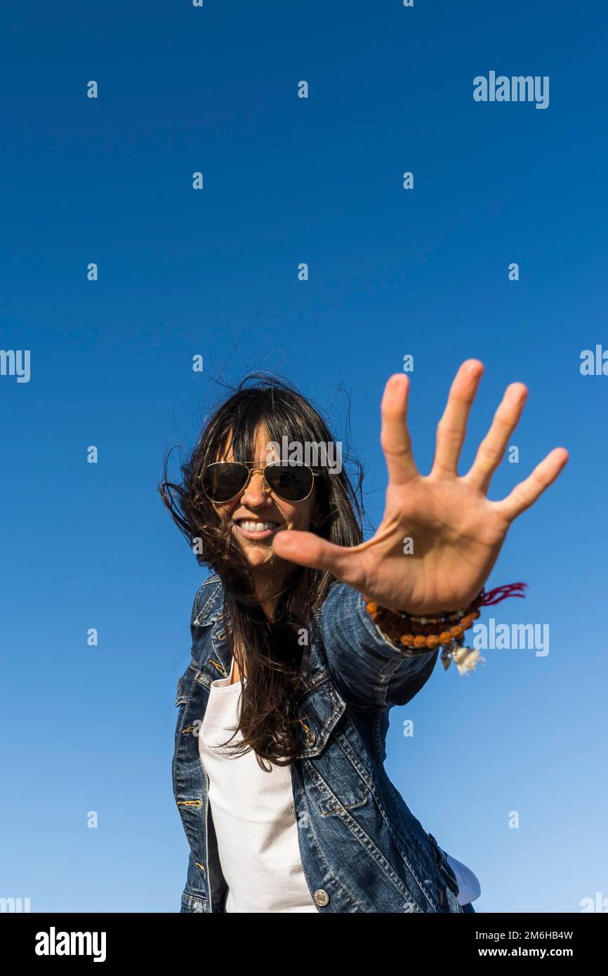 Low angle view of a similing woman while showing the palm of her hand. Blue sky background. Stop gesture Stock Photo