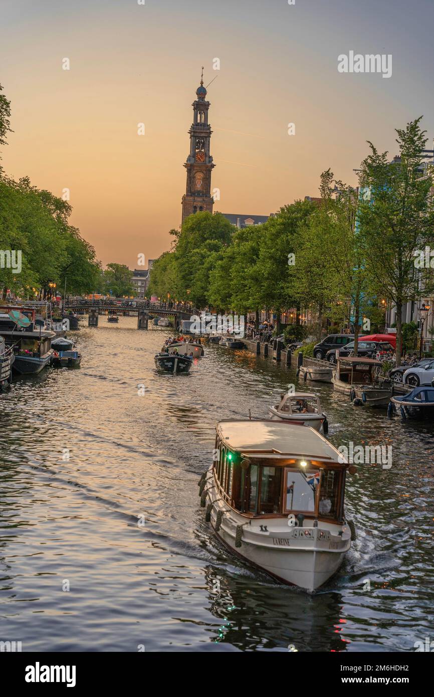 Boat cruising the canals at golden hour, church in the background, Amsterdam, Netherlands Stock Photo