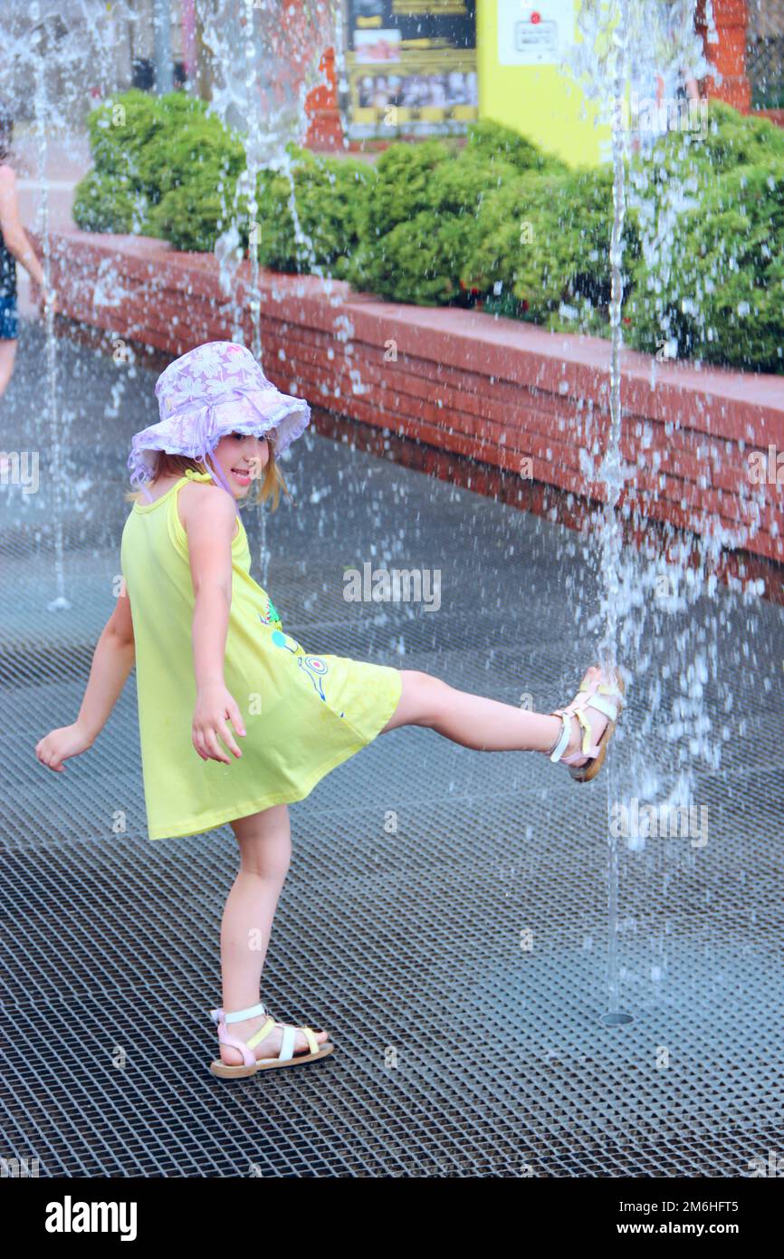 Little girl trying to touch water by foot in city fountains. People have a rest in city park with fo Stock Photo