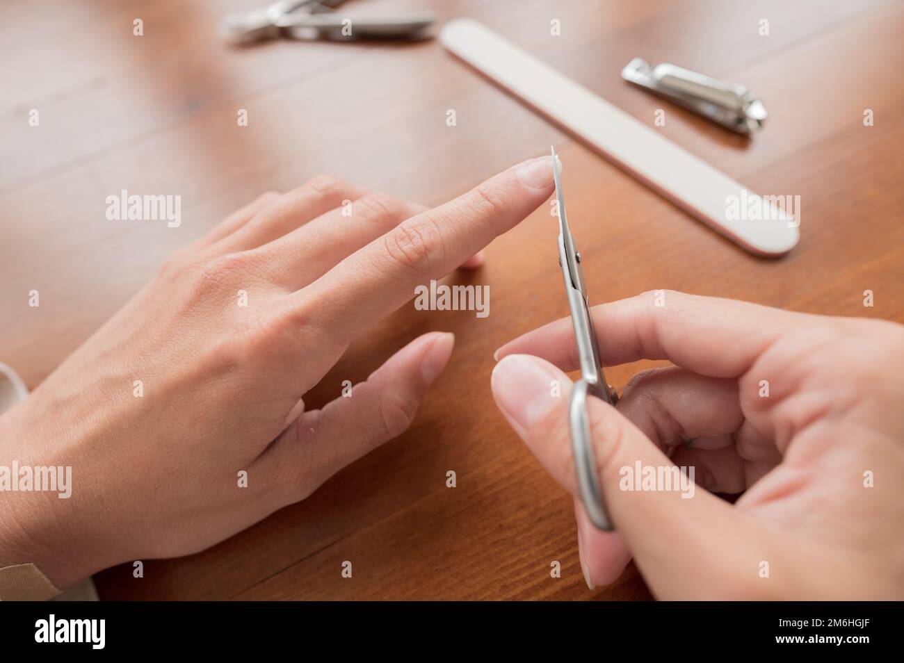 Close-up of hand of caucasian young woman doing manicure scissors, cut nail at home with nail supplies. Stock Photo