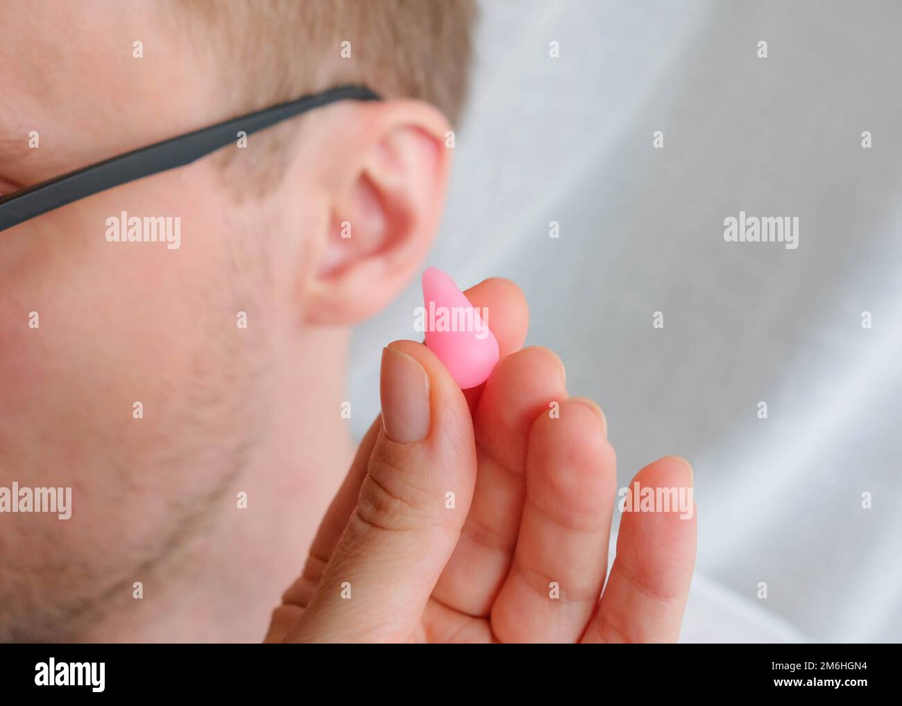Holds a pink wax earplug in his hand. Human ear in the background Stock Photo