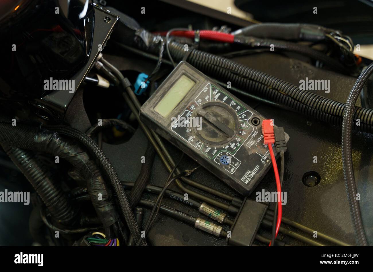 A mechanic using a multimeter checks the voltage level on a motorcycle