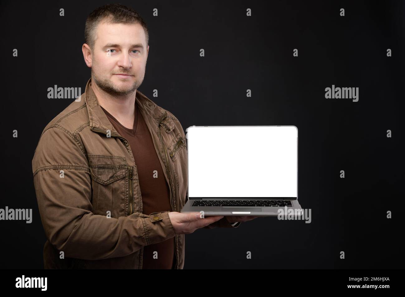 Attractive positive friendly Caucasian male holding laptop in hands presenting his cut out screen with copy space on black backg Stock Photo