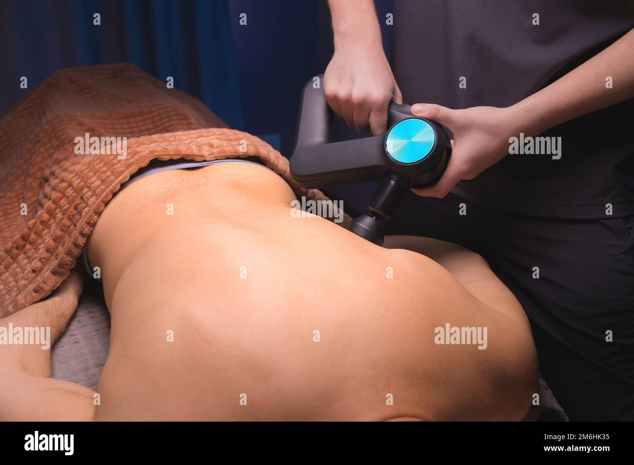 Close-up of a professional male masseur stimulates the back muscles of a male patient in a dark spa room for massage. Percussion Stock Photo