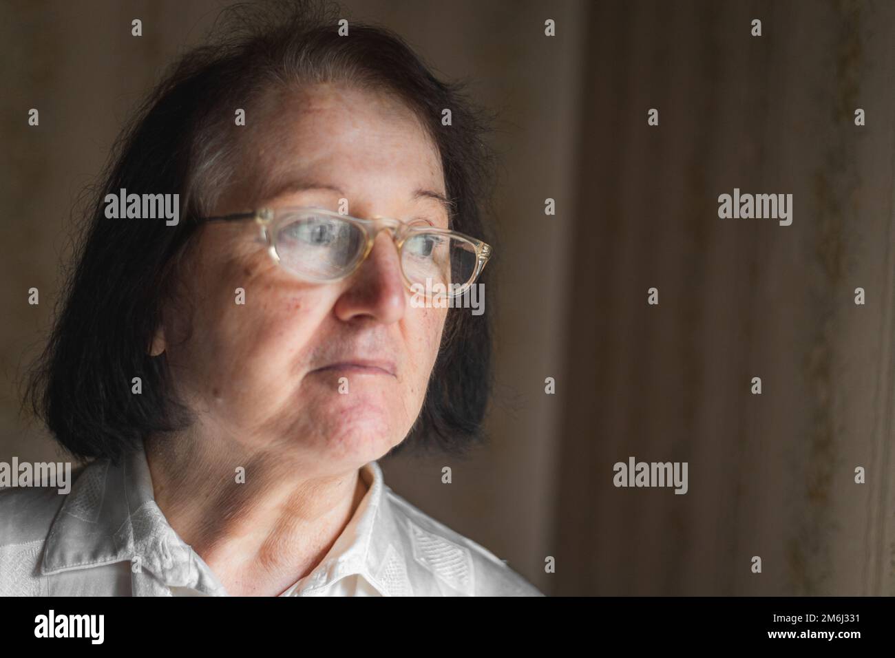 Elderly woman standing and looking through the window Stock Photo