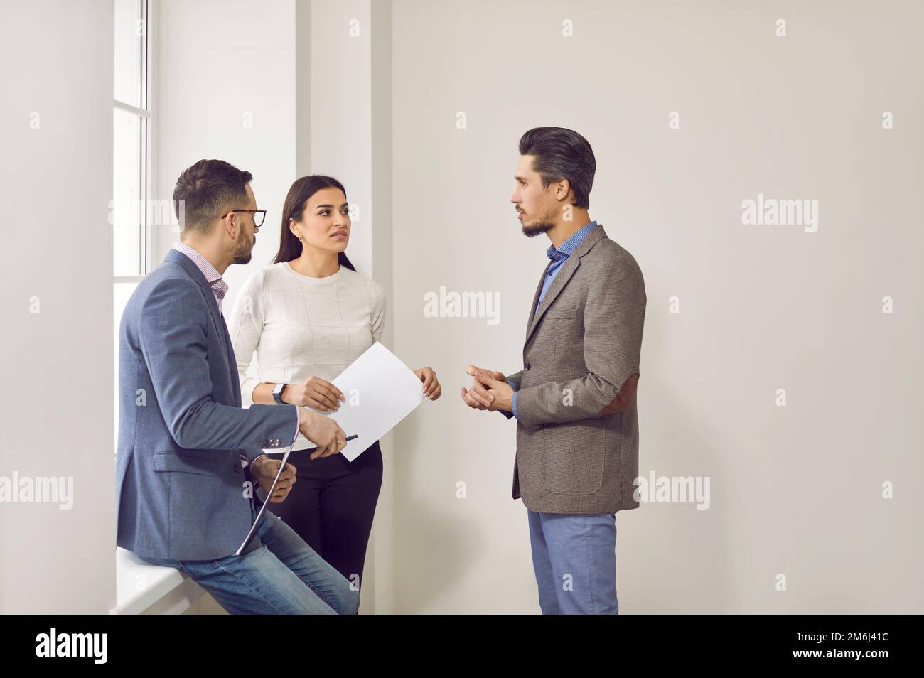 Group of three people having a discussion while standing together by an office window Stock Photo